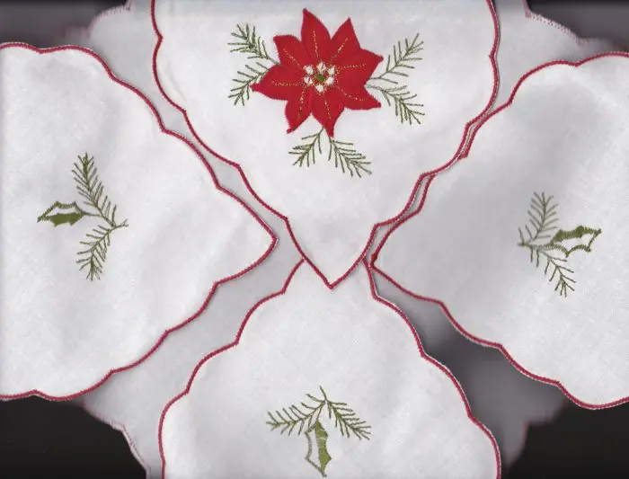 A scalloped white toast napkin with red trim, features a red poinsettia pattern. Each folded side has an embroidered green holly branch design. The center napkin features a red poinsettia with green holly branches.