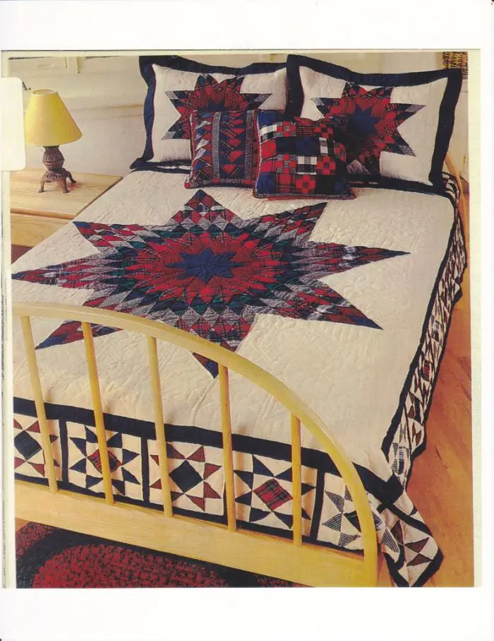 A bed with a wooden frame is adorned with the Flannel Tartan Lone Star hand quilted quilt, which features a large red, blue, and Cream star pattern. Matching pillows along with a small nightstand holding a yellow lamp are nearby, enhancing the cozy bedroom ambiance.