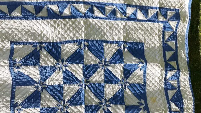 The Denim Star Hand-Quilted Quilt, made of 100% cotton, features a geometric pattern with blue and ivory triangles, squares, and diamond shapes, displayed on a grassy surface.