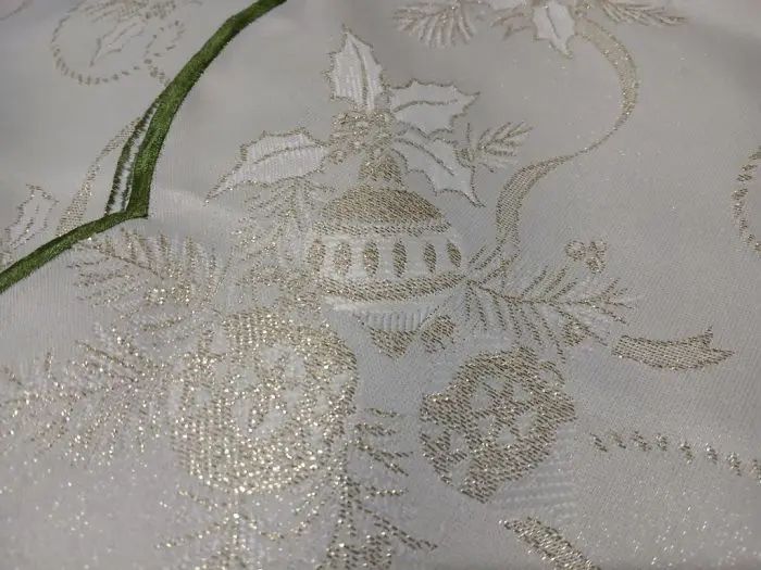 Close-up of the Sparkle Christmas Motifs Green and Golden Tablecloth, showcasing a festive design with gold thread embroidery. The pattern includes holly leaves, berries, and decorative ornaments, complemented by a dual tone green border edge accentuating the fabric.