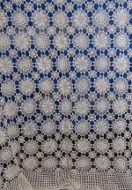 Snowflake Crochet BedCover-Ecru showcases an intricate design of crocheted lace with circular patterns set against a blue backdrop, featuring clusters of petal-like shapes that create a delicate and decorative appearance.