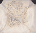 A close-up of the Elite Battemburg Lace Bun Warmer Cover shows delicate ecru cotton embroidery on sheer linen, with intricate floral and geometric openwork patterns.
