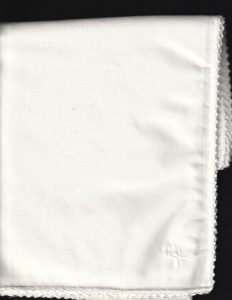 A neatly folded Wedding Ring WhiteWork Rose Tablecloth – Handcrafted Heirloom Lace, featuring delicate lace and rose motifs, set against a black background, evokes the timeless beauty of fine whitework embroidery.