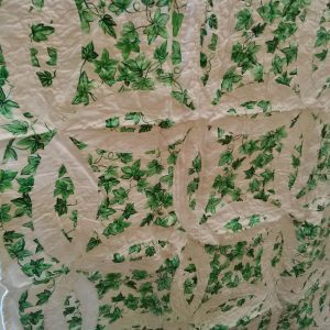 The Irish Green & White Double Wedding Ring Handmade Quilt features a detailed design with interlocking ring patterns and green leaves set against a white background, showcasing a visually intricate and textured fabric artwork.
