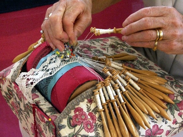 Hands creating intricate lace with bobbins and pins on a floral pillow, showcasing traditional techniques behind the "Wedding Handkie Bobbin Lace Vintage Handmade Keepsake Bride Tradition.