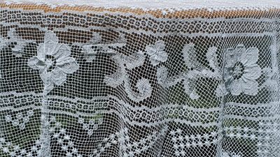 The Fine Table Linens: Tuscany Lace Hand Knotted Italian Modano Round tablecloth features intricate floral and geometric patterns on delicate mesh, allowing the surface beneath to show through.