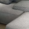 A close-up image of a sectional sofa in various shades of gray. The upholstery features a combination of plain and houndstooth patterns. A matching gray cushion is partially visible on top of the sofa.