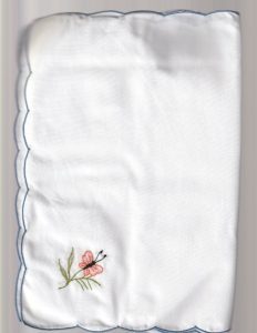 The Fine Table Linens – Embroidered Butterfly Meadow Tablecloth (50"x70") is a cotton blend tablecloth featuring blue scalloped edges and a pink butterfly with green leaves—ideal for summer picnics or elegant dining.