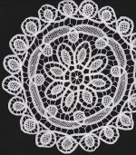 A designer-chosen wall decor piece featuring a circular, intricate white lace doily with floral and leaf patterns set against a dark background. This Home Decor DIY Framed Doilies Art showcases a central flower design encircled by smaller petal-like shapes.