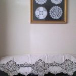 A Home Decor DIY Framed Doilies Art: Designer Choice Wall Decor is displayed on a beige wall above a sofa, which is covered with a white lace cloth featuring ornate patterns.