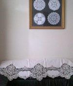 A Home Decor DIY Framed Doilies Art: Designer Choice Wall Decor is displayed on a beige wall above a sofa, which is covered with a white lace cloth featuring ornate patterns.