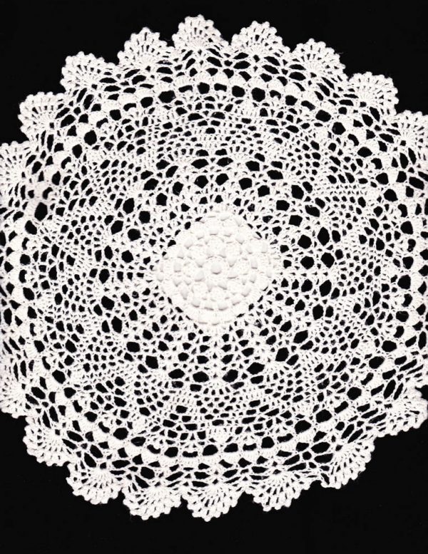 A white lace doily with intricate, symmetrical patterns is displayed against a black background. The doily has a circular shape with a detailed, floral-inspired design extending from the center outward. The edges are scalloped, adding to its delicate appearance.