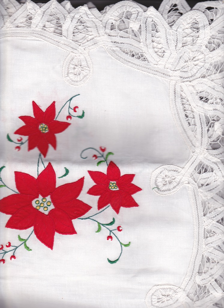 A white cloth with lace edging, featuring red poinsettia flowers and green embroidered stems and leaves. The design is delicate and festive, suitable for holiday decor.