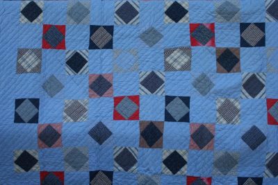 Introducing the MUSEUM FLANNEL PLAID PATCHWORK QUILT TICKING FABRIC BACKING, which showcases an intricate geometric pattern composed of diamond-shaped blocks in diverse shades of blue, red, and brown set against a light blue backdrop. Its sophisticated design incorporates both plaid and solid fabrics to form a harmonious and symmetrical layout.
