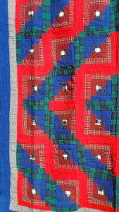 Introducing the Amish RED Barn Raising Handmade Flannel Quilt: a vibrant masterpiece showcasing a geometric patchwork pattern. It features red, blue, and green hues along with plaid squares arranged in concentric formations for a visually striking effect.