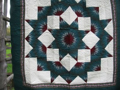 The Nostalgia 1980s Donna Sharp Broken Star Original Quilt hangs on a wooden fence, showcasing complex geometric patterns in dark green, ivory, and burgundy star shapes with intricate stitching.