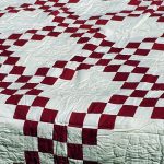 The Irish Chain Quilt in burgundy features a red and white checkerboard pattern with intersecting diagonal lines, creating a lattice-like look that adds a traditional and cozy feel to the bedding.