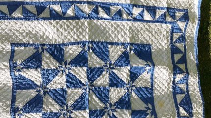 The Denim Star Hand-Quilted Quilt, made of 100% cotton, features a geometric pattern with blue and ivory triangles, squares, and diamond shapes, displayed on a grassy surface.