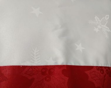 Close-up of the Christmas Red & Silky Ivory Jacquard Damask Tablecloth, showcasing a creamy ivory background with subtle star and bell patterns, accented by a red border adorned with holly and berry designs, making it perfect for a festive holiday theme.