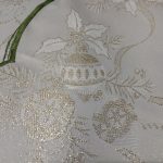 Close-up of the Sparkle Christmas Motifs Green and Golden Tablecloth, showcasing a festive design with gold thread embroidery. The pattern includes holly leaves, berries, and decorative ornaments, complemented by a dual tone green border edge accentuating the fabric.