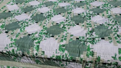 The Sparkling Green & White Courthouse Steps Prairie Point Border quilt features a vibrant, intricate patchwork design with floral and checkered patterns, combining squares and circular motifs.