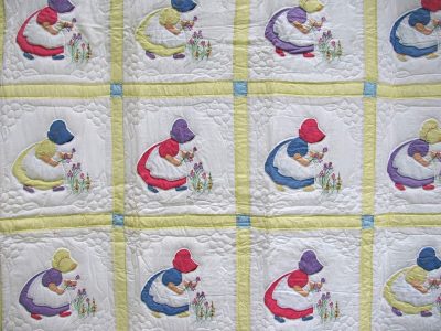 The Sun Bonnet Sue or Little Dutch Girl Hand Appliqué Quilt showcases panels of girls in bonnets holding flowers, dressed in red, blue, purple, yellow, and green. The design is set on a white background with yellow and blue borders.