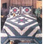 A cozy bedroom showcases a metal-frame bed adorned with the Log Cabin Lone Star 1980 American Pacific Design quilt and pillows in red, blue, and white star patterns. The room features a decorative rug, potted plant, and bedside table with cheerful plush toys.