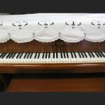 A close-up of a piano keyboard, with the Cluny Lace Piano Cover Scarf with Richelieu Embroidery (90"x30") partially covering the uptight pisno top.