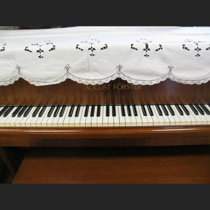 A close-up of a piano keyboard, with the Cluny Lace Piano Cover Scarf with Richelieu Embroidery (90"x30") partially covering the uptight pisno top.