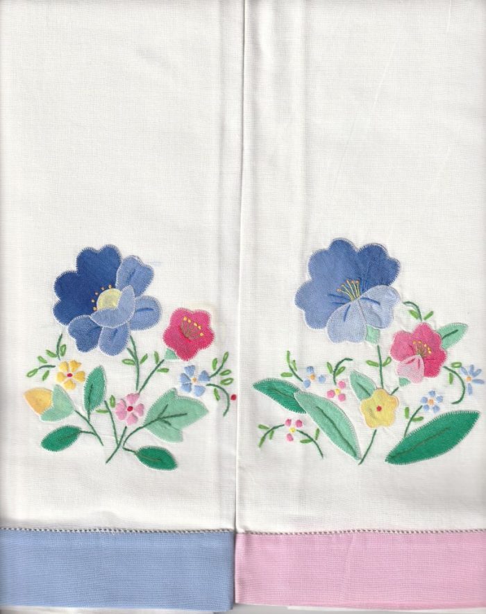 Set of 2 Hand-Stitched Appliqué Guest Towels in white, each with colorful embroidered flowers and green leaves. One has a blue hemstitch pastel border, the other pink; both share identical floral designs.