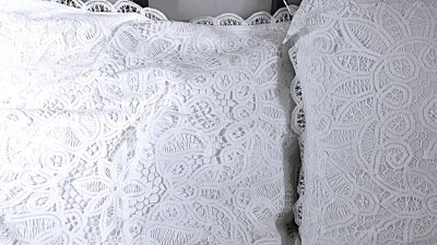 Two white decorative pillows with intricate lace patterns and scalloped edges are placed next to each other on a bed.