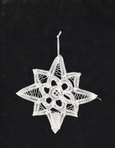 The Wish Upon a Star Handmade White Battenburg Lace Christmas Ornament, a 6-point star doily with a hanging loop, is displayed against a black background.