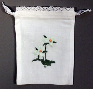 A white drawstring pouch with lace trim, decorated with embroidered white lilies and green leaves in the center.