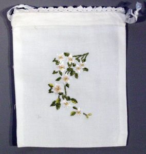 A white drawstring bag with a lace-trimmed top, featuring an embroidered British Columbia Provincial Flower Design Pacific Dogwood in the center.