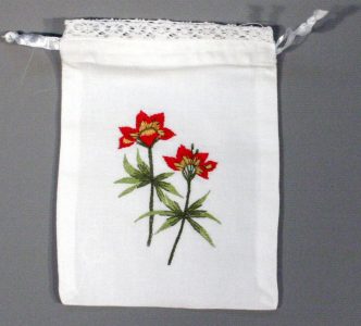 A small white drawstring bag with lace trim at the top, featuring two red and yellow embroidered flowers with green stems and leaves on the front.